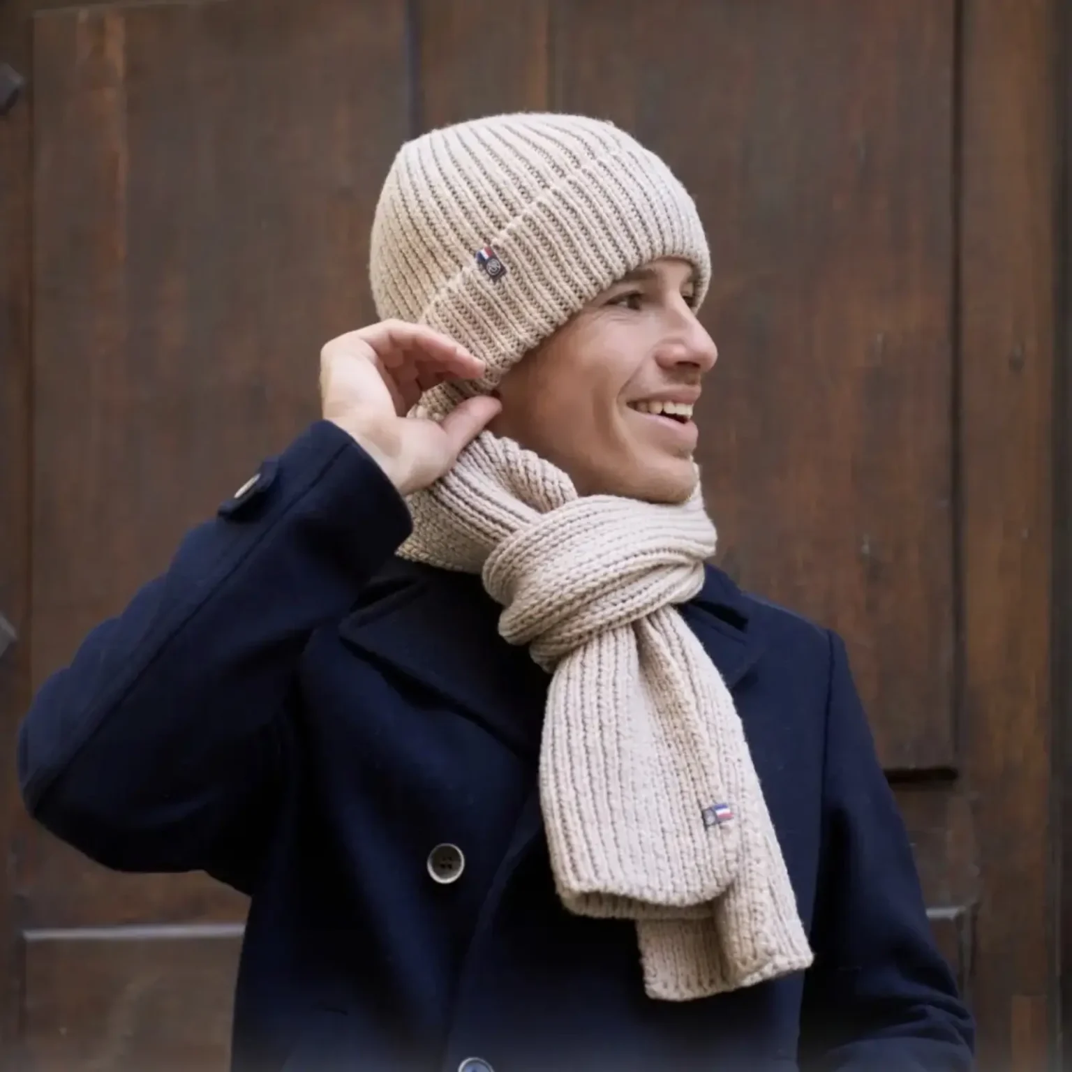 Bonnet CLAIRE, beige en maille côtelée porté par un homme dans un environnement urbain extérieur.