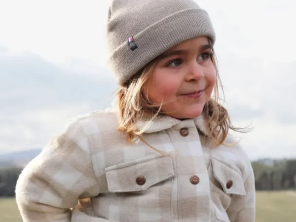 Bonnet en maille côtelée couleur beige, porté avec une tenue hivernale. Sa teinte douce et naturelle s'accorde facilement avec les vêtements d'hiver. Sa coupe classique apporte une finition sobre et confortable.