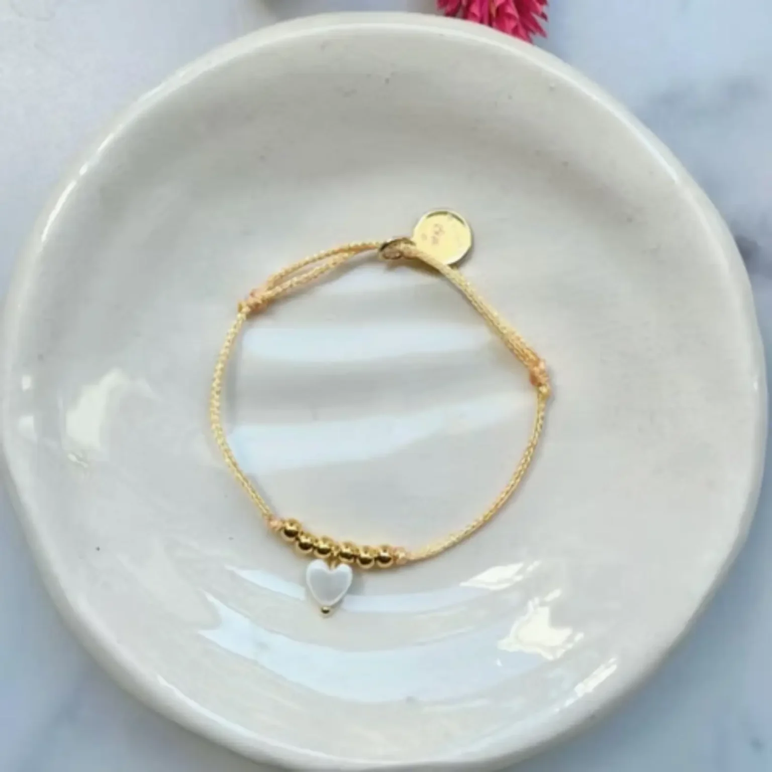 Bracelet enfant Les Câlines corail avec cordon fin et petit cœur doré.