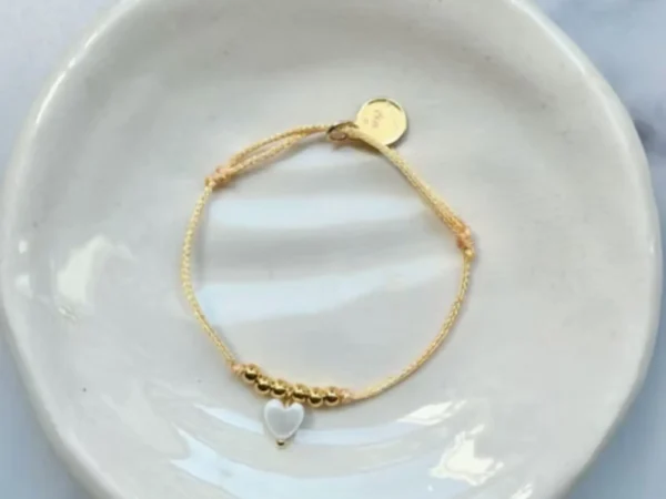 Bracelet enfant Les Câlines corail avec cordon fin et petit cœur doré.